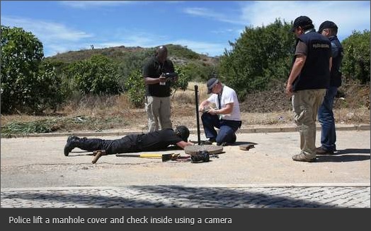 Police lift a manhole cover and check inside using a camera